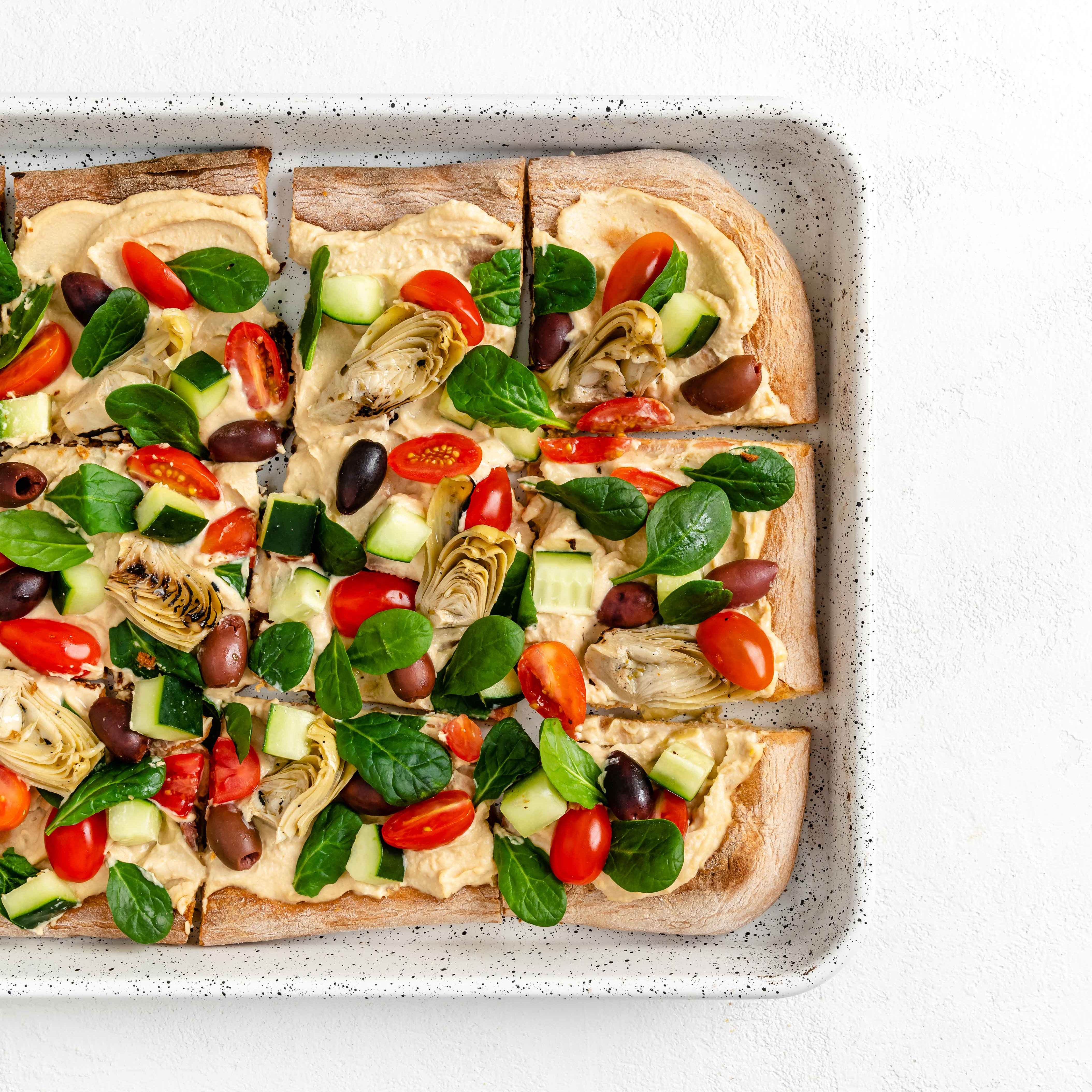 Pizza topped with hummus, tomatoes, olives, and basil